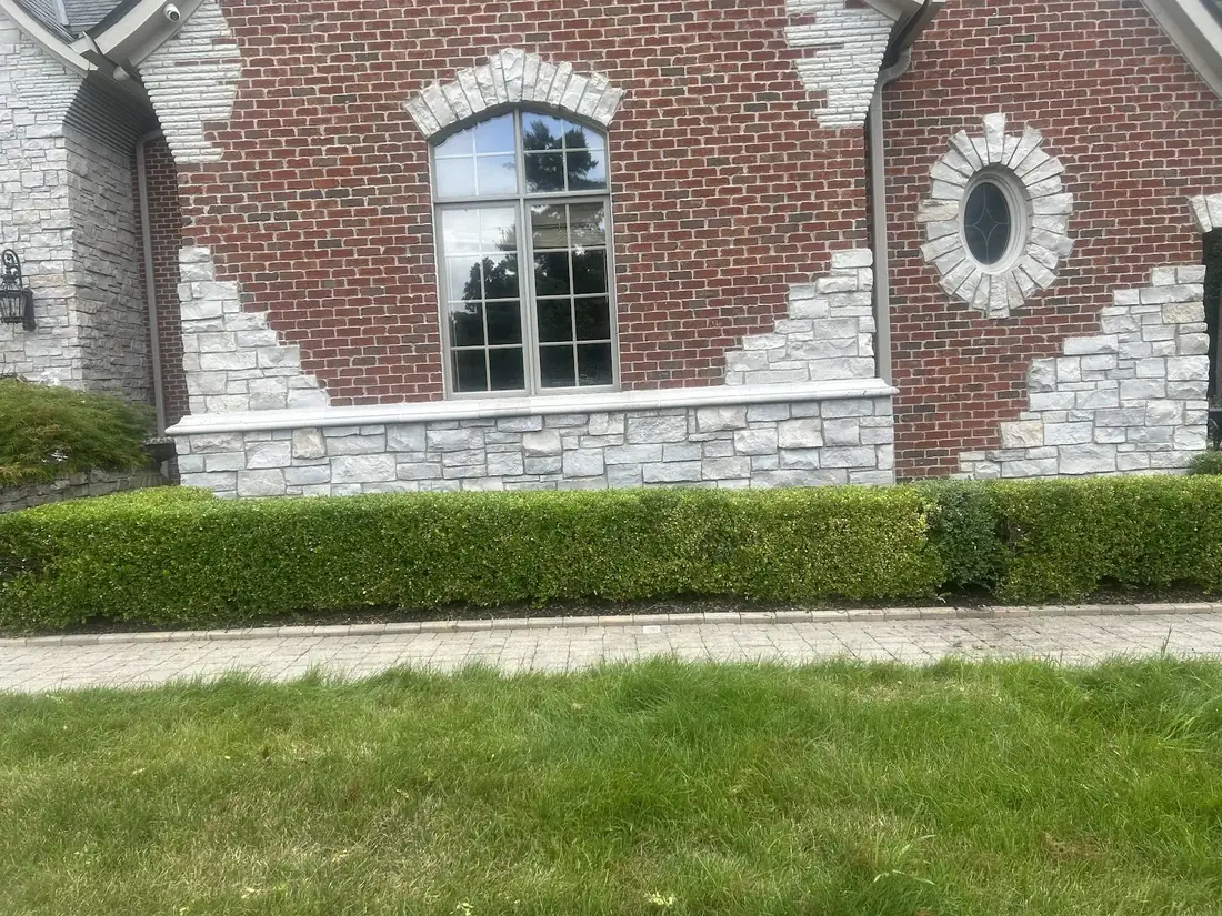 Neatly trimmed hedges along a paver walkway at a Troy, MI home landscaped by AJC Landscaping